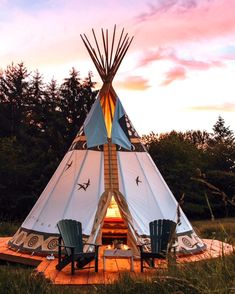 a teepee sitting in the grass with chairs around it