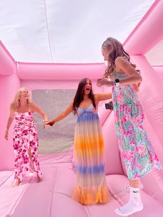 two women in colorful dresses are standing on an inflatable structure and one woman is holding the hand of another woman