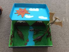 an animal habitat made out of cardboard with fake grass and water in the bottom part