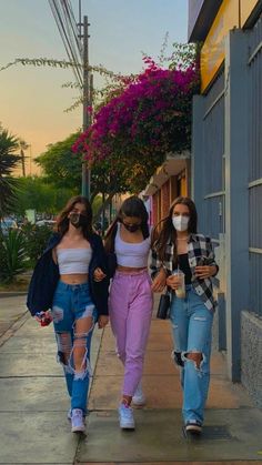 three girls walking down the sidewalk wearing face masks and ripped denims in front of a building