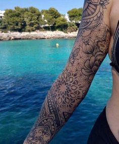 a woman with tattoos on her arm standing next to the ocean