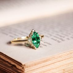 an emerald and diamond ring sitting on top of a book with pages in the background