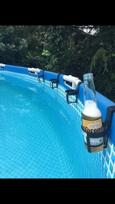 a beer bottle sitting on top of a blue swimming pool next to a lush green forest