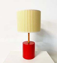 a red table lamp with a yellow and white striped shade on the top of it