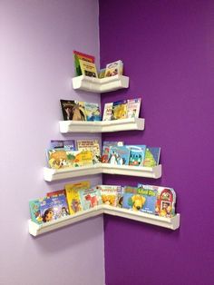 three white shelves with books on them against a purple wall in a children's room