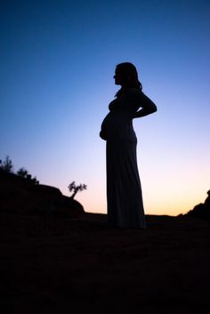 a pregnant woman standing in the desert at sunset