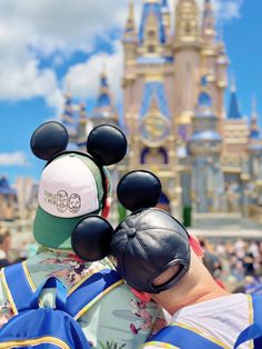 two people wearing mickey mouse ears and hats in front of a castle at disney world