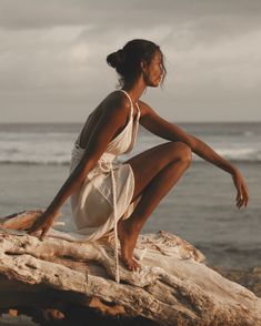 a woman sitting on top of a wooden log near the ocean