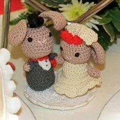 two small crocheted figurines sitting on top of a white plate next to flowers