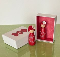 a red figurine next to a white box with hearts on it and a pink background