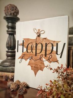 a wooden sign that says happy fall on it next to pine cones and acorns