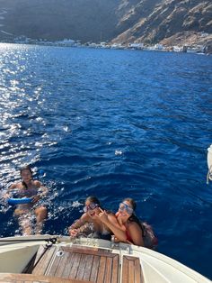 two people on a boat in the water with mountains in the background and one person wearing goggles