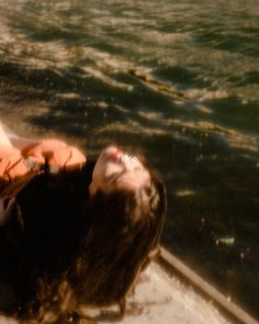 a woman laying on top of a boat in the water with her eyes closed and hair blowing back