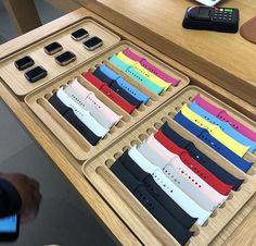 a wooden table with several different colored watches on it and a person using a cell phone