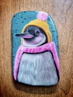 a painted penguin wearing a yellow hat and pink scarf on top of a wooden table