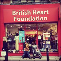 two people walking past a british heart foundation store with their baby in a stroller