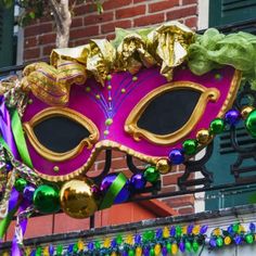 a mardi gras mask hanging from the side of a brick building with green and gold decorations