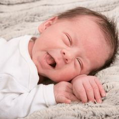 a smiling baby laying on top of a bed next to a white blanket with his eyes closed