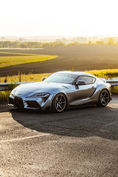 a silver sports car parked on the side of a road next to a grassy field