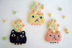 three cookies decorated to look like cats with flowers on their heads and ears, sitting next to each other