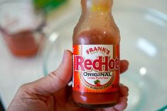 a hand holding a bottle of red hot sauce