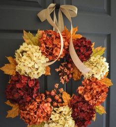 a wreath hanging on the front door with autumn leaves and hydrangeas around it