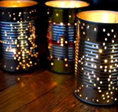 three tin cans with lights on them sitting on a wooden table next to each other