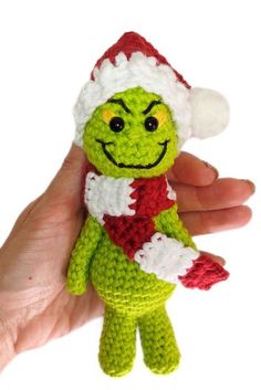 a hand holding a small green crocheted stuffed toy wearing a santa hat and scarf