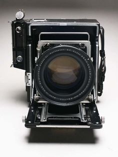 an old fashioned camera sitting on top of a white surface with a lens attached to it