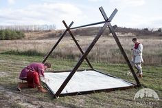 two people standing next to a structure made out of sticks and snow in the middle of a field