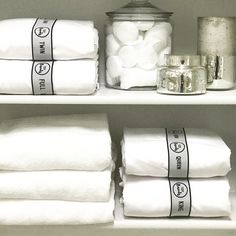 towels and other items are on shelves in a room with white linens, jars and silver canisters