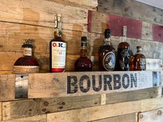 several bottles of liquor are lined up on a wooden shelf with the word bourbon painted on it