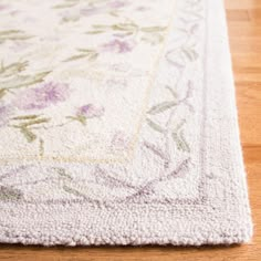 a white rug with purple and green flowers on the bottom is sitting on a wooden floor