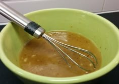 a green bowl filled with brown liquid and whisk