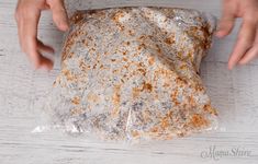 a person holding a piece of bread wrapped in plastic on top of a white table