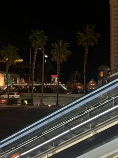 an escalator with palm trees and buildings in the background at night, as seen from across the street