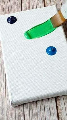 a paintbrush is being used to paint a square piece of white paper with blue and green buttons