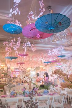 several umbrellas hanging from the ceiling in a room filled with tables, chairs and flowers