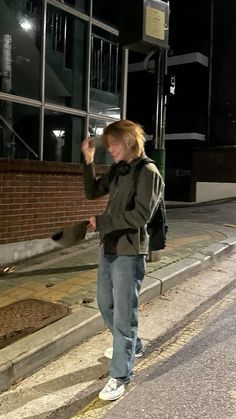 a young man standing on the side of a road next to a building at night