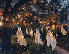 halloween decorations in the yard with lights strung from trees and hanging ghost costumes on them