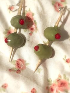 three green and red pins with cherries on them sitting on a white fabric covered tablecloth