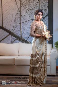 a woman standing in front of a couch wearing a sari and holding a bouquet