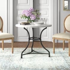 two chairs and a table with flowers on it in front of a white door way