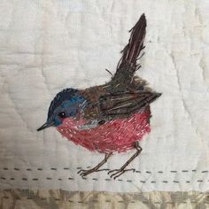 a small bird is sitting on the edge of a piece of white fabric with red and blue feathers