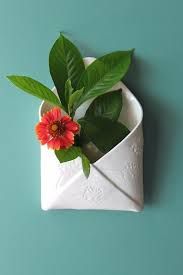 a red flower in a white vase with green leaves on a blue wall behind it