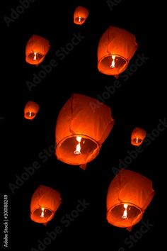 many orange lanterns floating in the air at night with lights glowing on them and one lit up