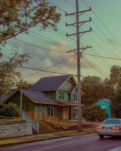 a car is driving down the street in front of some houses and power lines at sunset