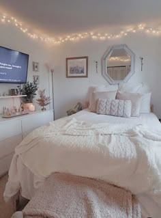 a bedroom with white bedding and string lights on the ceiling, along with a flat screen tv