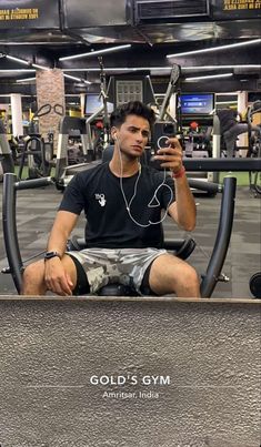 a man sitting on top of a bench in a gym holding a cell phone to his ear