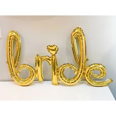 gold foil balloons spelling the word love on top of a white table with a wall in the background